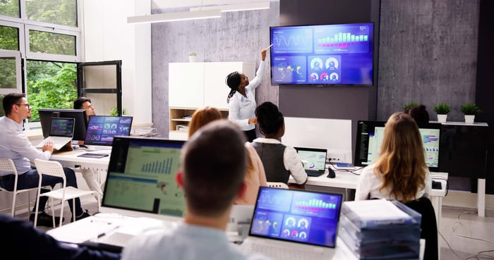 Person screen mirroring from a computer to a TV in a room with his peers